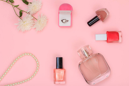 盒子上有金色戒指，珠子，香水瓶，指甲油瓶和粉红色背景上的花。女性化妆品及辅料..上景。