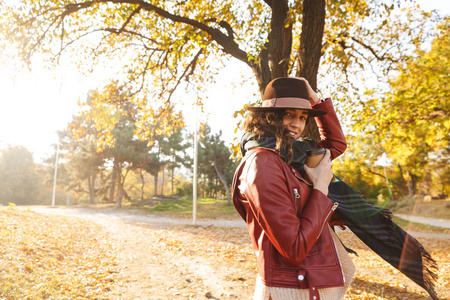 美丽的年轻女子戴着帽子在公园散步，秋天拿着一杯外卖咖啡