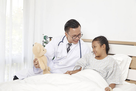 医学概念。 医生拿着玩具熊和小女孩在医院里开心地笑着检查