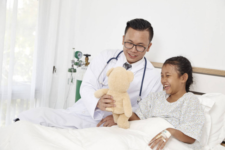 医学概念。 医生拿着一只玩具熊和一个小女孩在医院里检查