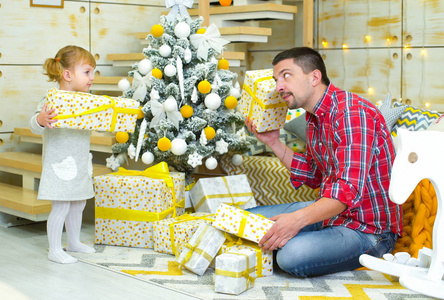 年轻的父亲和幼儿女儿在家里装饰圣诞树附近探索礼品盒