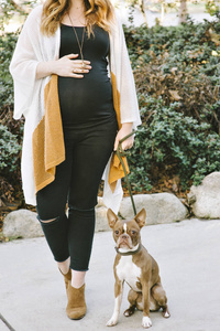 孕妇站在她的宠物波士顿猎犬旁边，双手放在腹部