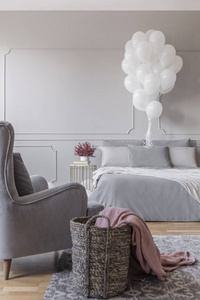 灰色时尚卧室的生日装饰，舒适的床，时髦的扶手椅和篮子，粉红色的毯子，真实的照片，复制空间在空墙上。