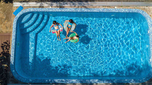 家庭游泳池，空中无人机，从上面看到快乐的母亲和孩子在充气环形甜甜圈上游泳，在度假胜地的家庭度假热带假日在水中享受乐趣。