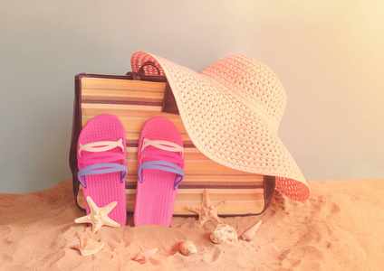 拖鞋袋夏季帽子和贝壳在沙滩上的蓝色背景。 暑假概念。