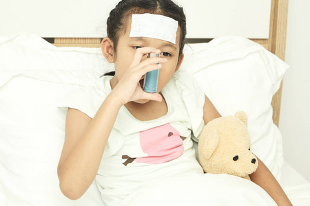 亚洲女孩坐在床上，用支气管扩张器吸入器缓解哮喘症状