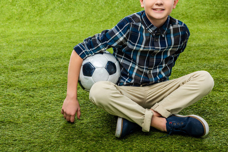 微笑的男孩捧着足球坐在草坪上