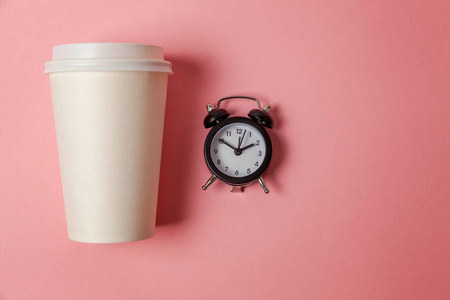 简单的平躺设计，纸，咖啡杯和闹钟在粉红色的糊彩彩色时尚背景。 外卖饮料和早餐饮料。 早上好，醒来的概念。 顶部视图复制空间
