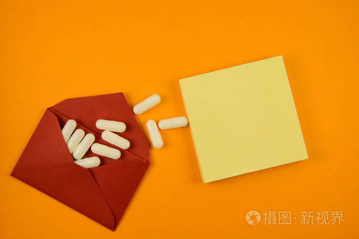 红色信封中的白色药丸和橙色背景中的黄色棍子笔记