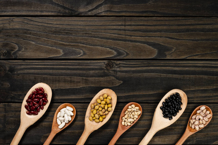 木制勺子里豆子的多样性。 黑色的木头背景。