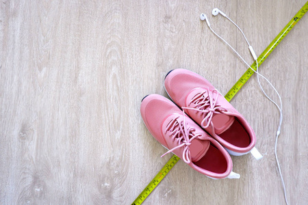 健身配件一双粉红色运动鞋与白色耳机耳机和测量磁带的木材。 女人运动服。 运动鞋的顶部视图隔离在木制背景复制空间上。