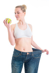 穿着大裤子和苹果的漂亮女孩。 运动健身和饮食理念。 孤立于白色背景
