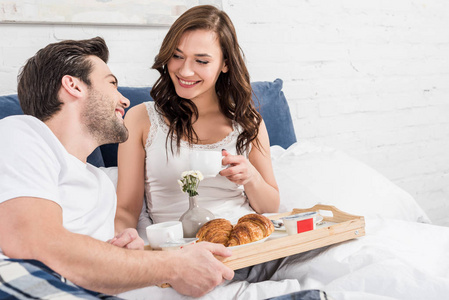微笑的夫妇躺在床上，早上吃早餐