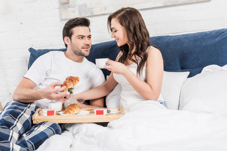 一对夫妇躺在床上，早上在家吃早餐