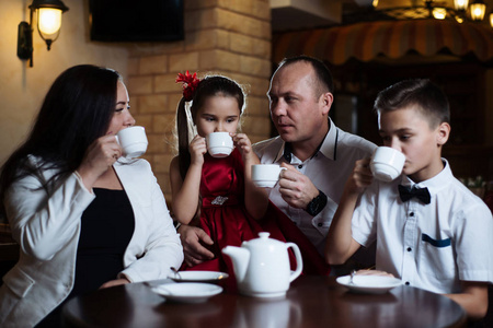 一家人聚集在一家咖啡馆里。妈妈, 爸爸, 小女儿和儿子喝茶。他们在一起很幸福。愉快的家庭午餐概念