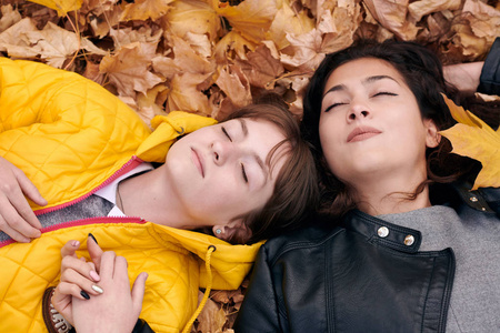 美丽的女人和十几岁的女孩在秋天公园摆姿势。他们躺在落叶上。秋天的美景。
