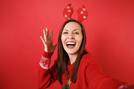 特写自拍的快乐年轻圣诞老人女孩在有趣的装饰鹿角上升的手孤立在明亮的红色背景。 新年快乐，2019年庆祝节日聚会的理念。 模拟复制