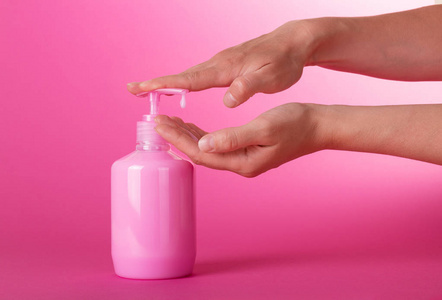 s hands dial the fragrant liquid soap on a pink background