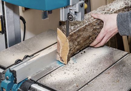 木工车间的工人用带锯把原木切成板。 细木工。 生木木工艺品。 在工厂工作。