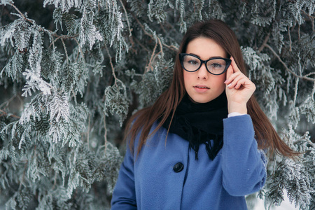 圣诞树旁边是穿着围巾和蓝色外套的快乐年轻女子的肖像。黑眼镜