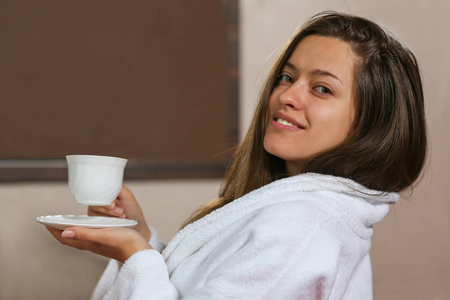 这位美丽的女人穿着浴袍，早上在酒店房间喝茶。