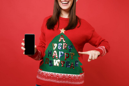 裁剪的图像微笑圣诞老人女孩指着食指在手机上与空白空屏隔离在红色背景。 新年快乐，2019年庆祝节日聚会的理念。 模拟复制空间