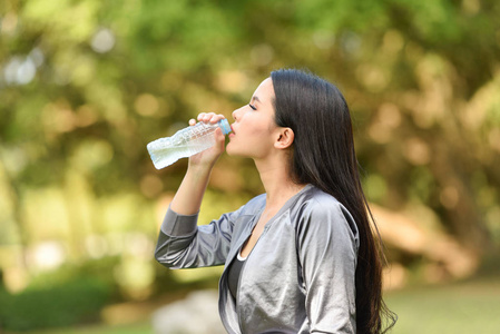 女人饮水瓶健康观念微笑的年轻女孩放松运动，手拿水瓶喝水，在花园公园背景下户外快乐的女人。