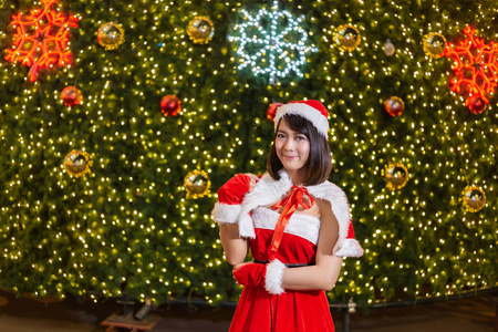 快乐的微笑圣诞老人女孩是可爱的红色西装与圣诞树背景庆祝圣诞节和快乐的新年节日。