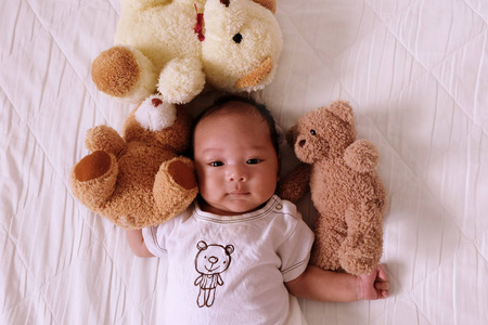亚洲可爱的婴儿新生的微笑和快乐的好心情在床上与泰迪熊顶视图。