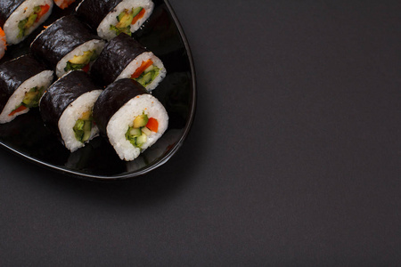 寿司卷在诺里海藻片与鳄梨和红鱼在陶瓷盘子。顶部视图，黑色背景和复制空间。