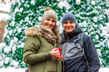 年轻夫妇在冬季圣诞节市场。 年轻的男人和女人站在雪地上，背景是圣诞树。 寒假的浪漫关系和快乐