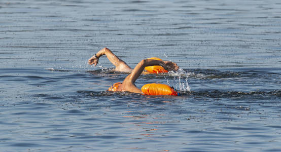 两名男性游泳运动员正在长岛的户外游泳，他们的浮浮装置漂浮在他们身后，以确保安全。