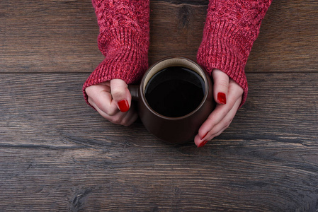 s hands in a red sweater and a cup of coffee on a wooden backgro