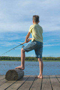 男孩在码头上靠蓝天和湖后景色钓鱼
