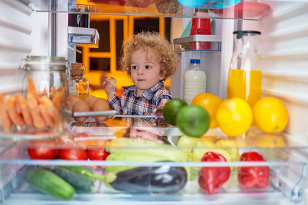蹒跚学步的孩子从冰箱里偷食物。 从冰箱边上拍的照片。