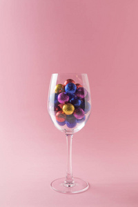 粉红色背景上酒杯中的彩色糖果。 最小的假期概念。