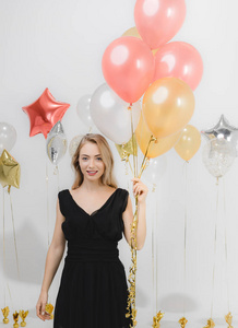 美丽的年轻白种人女士穿着黑色的裙子，开心的微笑着拿着五颜六色的气球在有趣的聚会上，工作室的肖像拍摄白色背景。