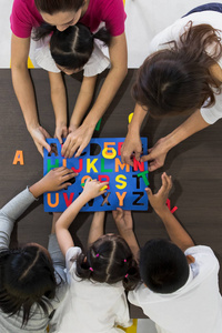 平躺镜头的亚洲教师玩彩色字母拼图玩具与亚洲学生一起概念为课堂。