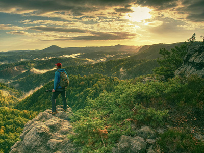 高大的摄影师，戴着棒球帽和三脚架，手里拿着相机，站在岩石的视点上，俯视着深深的雾蒙蒙的山谷