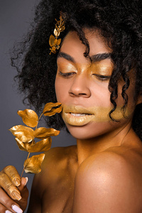 非洲裔美国妇女，她的身体在黑暗的背景下有金色的油漆