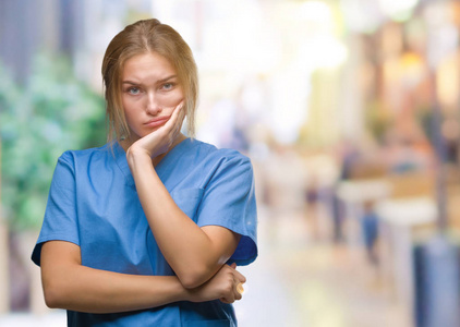 年轻的高加索护士女士穿着外科医生制服，在孤立的背景下思考，看起来疲惫，厌倦了交叉双臂的抑郁问题。