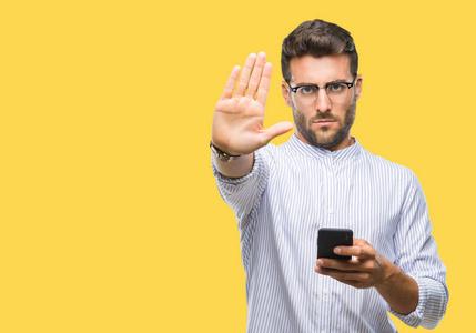 年轻的帅哥用智能手机在孤立的背景上发短信，张开手做停止标志，严肃自信的表情防御手势