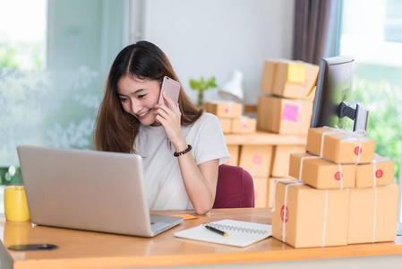 亚洲女人在笔记本电脑和办公室电话上使用互联网时很享受自己。 商业和营销以及兼职概念。 网上购物和商业成功主题。 快乐的心情做工作