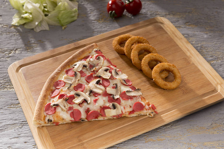 近距离观看一块意大利比萨饼和油炸洋葱圈在木切割板上
