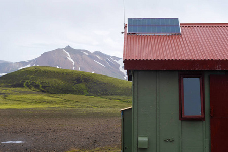 国家公园的旅游业。外面的一张小绿房子的照片，红色屋顶上有太阳能电池板，电力从发电机站起来，映衬着美丽的风景