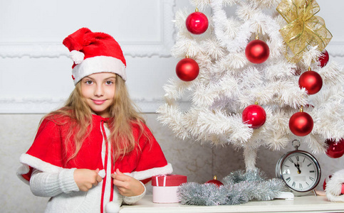 珍爱人的假期活动。孩子在圣诞老人帽子装饰圣诞树。家庭传统概念。用红色的球饰品装饰圣诞树的儿童。装饰圣诞树的女孩孩子