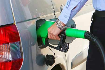 在加油站的特写镜头里，女人把汽油装满了她的车。 女人手拿着燃油泵在车站。