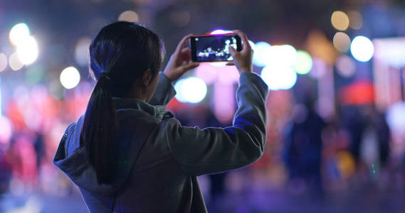 女人晚上在街上的智能手机上拍照