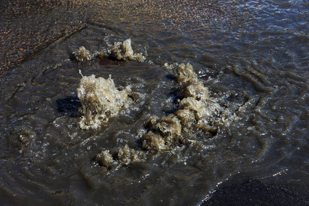 水从道路污水舱口流出。 污水的排水喷泉。 污水系统事故。 肮脏的污水在道路上流动喷泉。 从舱口流出的水