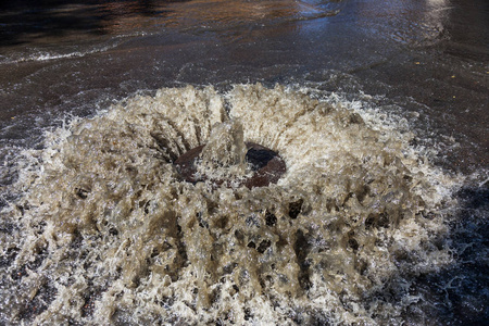 水从道路污水舱口流出。 污水的排水喷泉。 污水系统事故。 肮脏的污水在道路上流动喷泉。 从舱口流出的水